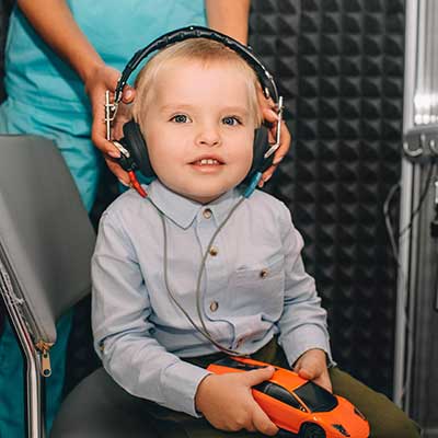 A toddler having hearing tested in a hearing booth.